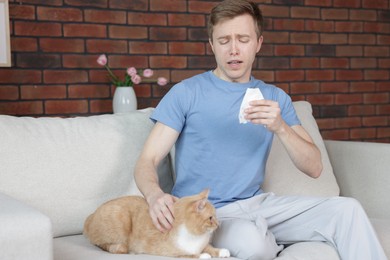 Photo of Man suffering from allergy with his cat on sofa at home