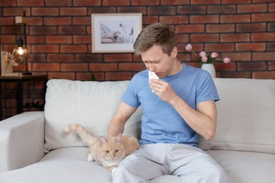 Photo of Man suffering from allergy with his cat on sofa at home