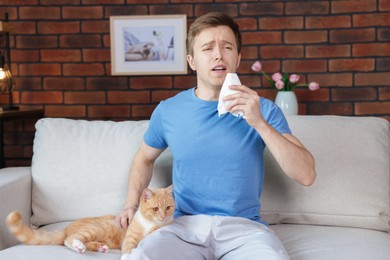 Photo of Man suffering from allergy with his cat on sofa at home