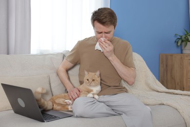 Photo of Man suffering from allergy with his cat on sofa at home