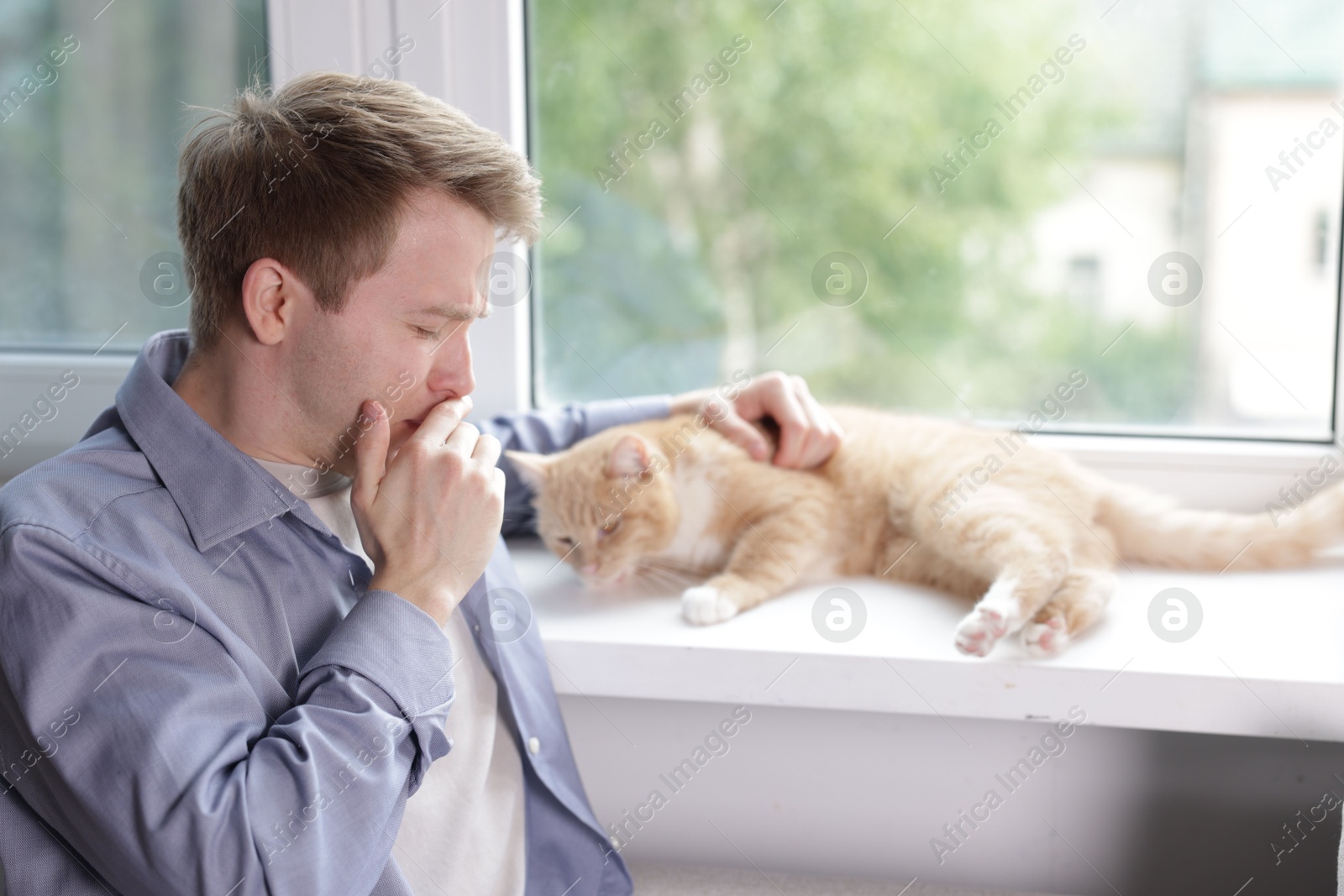 Photo of Man suffering from allergy with his cat near window at home
