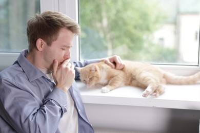 Photo of Man suffering from allergy with his cat near window at home