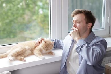 Photo of Man suffering from allergy with his cat near window at home