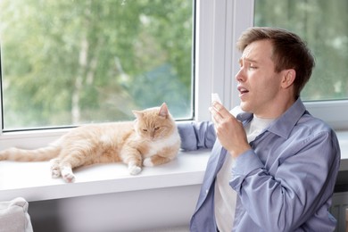 Photo of Man suffering from allergy with his cat near window at home