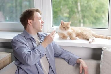 Photo of Man suffering from allergy with his cat near window at home