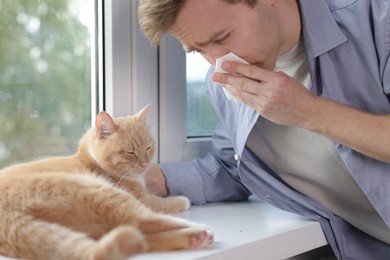 Photo of Man suffering from allergy with his cat near window at home