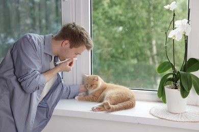 Photo of Man suffering from allergy with his cat near window at home