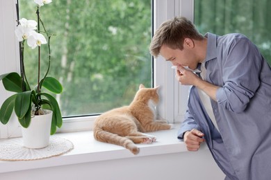 Photo of Man suffering from allergy with his cat near window at home