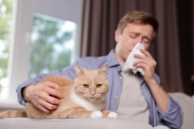 Photo of Man suffering from allergy with his cat on sofa at home, selective focus