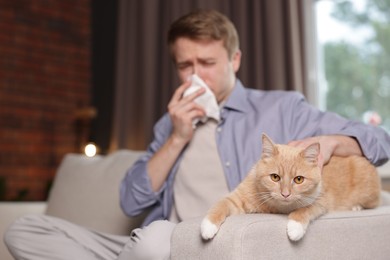 Photo of Man suffering from allergy with his cat on sofa at home, selective focus. Space for text