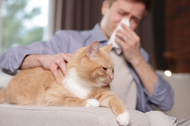 Photo of Man suffering from allergy with his cat on sofa at home, selective focus