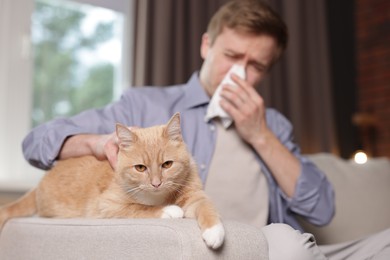 Photo of Man suffering from allergy with his cat on sofa at home, selective focus