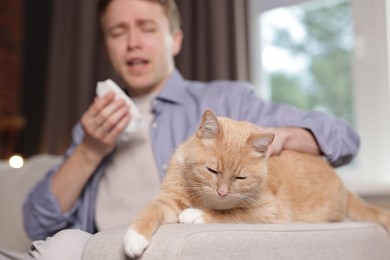 Photo of Man suffering from allergy with his cat on sofa at home, selective focus