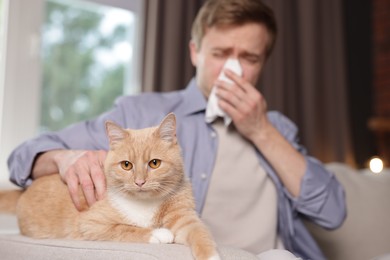 Photo of Man suffering from allergy with his cat on sofa at home, selective focus