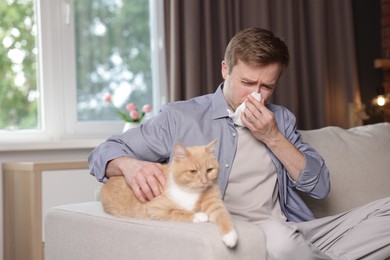 Photo of Man suffering from allergy with his cat on sofa at home