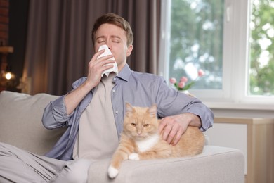 Photo of Man suffering from allergy with his cat on sofa at home