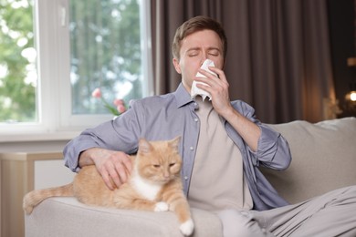 Photo of Man suffering from allergy with his cat on sofa at home
