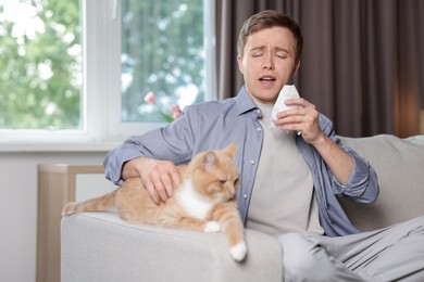 Photo of Man suffering from allergy with his cat on sofa at home