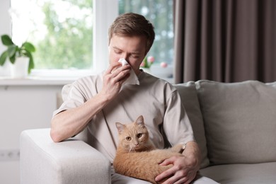Photo of Man suffering from allergy with his cat on sofa at home