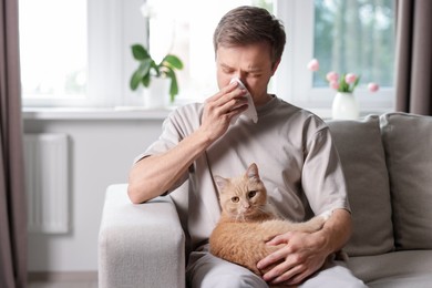 Photo of Man suffering from allergy with his cat on sofa at home