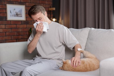 Photo of Man suffering from allergy with his cat on sofa at home
