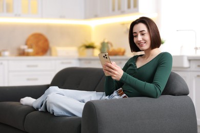 Photo of Woman using modern smartphone on sofa at home. Space for text