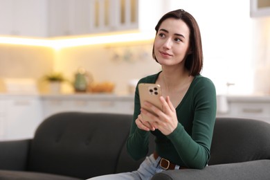 Photo of Woman using modern smartphone on sofa at home. Space for text