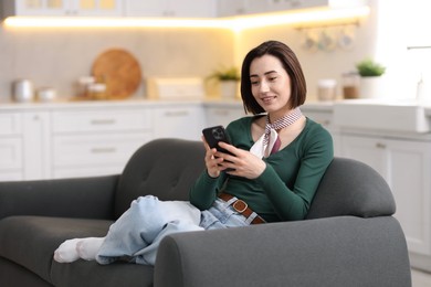 Photo of Woman using modern smartphone on sofa at home