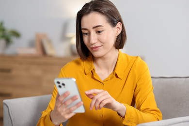 Photo of Woman using modern smartphone in armchair at home