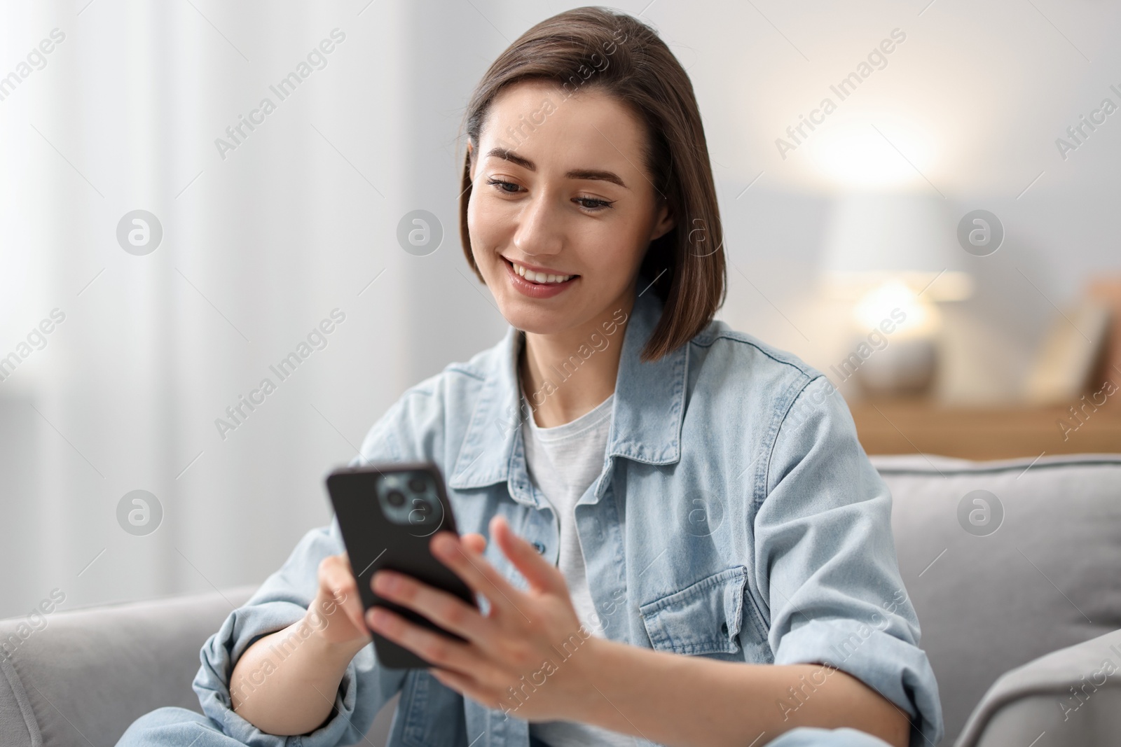 Woman using modern smartphone in armchair at home Photo of Woman using modern smartphone in armchair at home