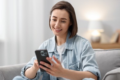 Photo of Woman using modern smartphone in armchair at home