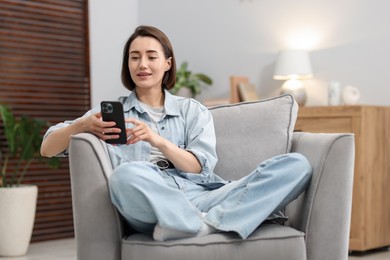 Photo of Woman using modern smartphone in armchair at home