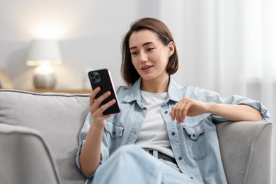 Photo of Woman using modern smartphone in armchair at home