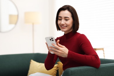 Photo of Woman using modern smartphone on sofa at home. Space for text
