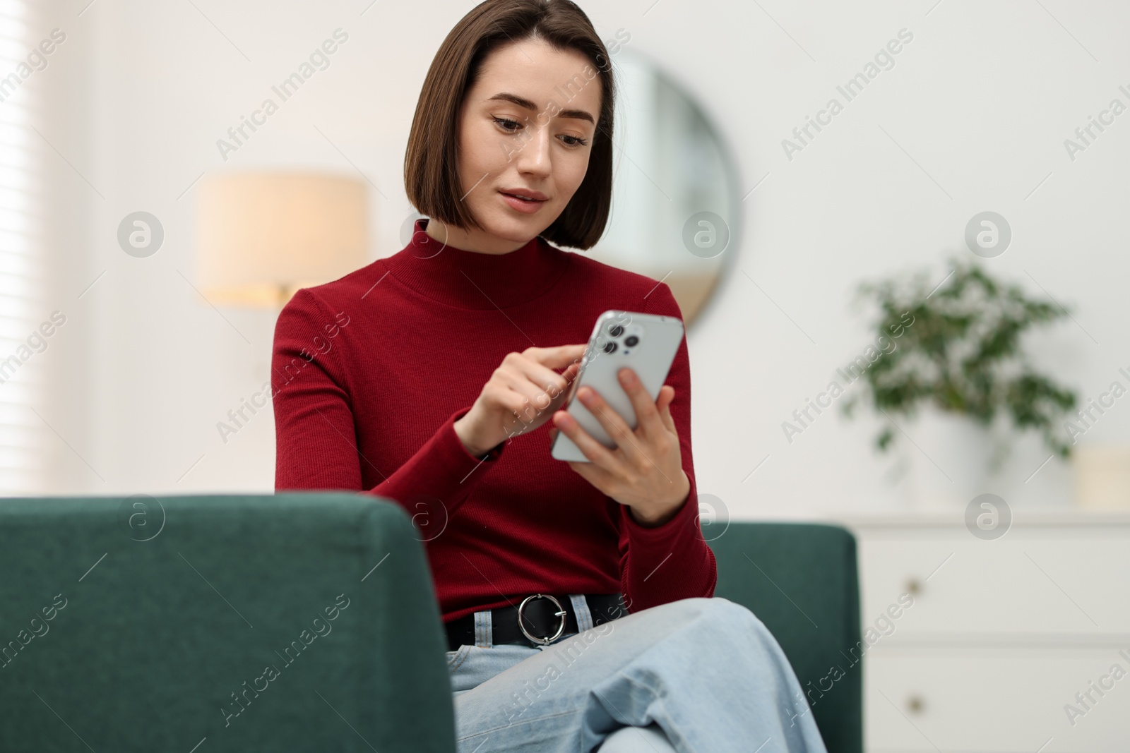 Woman using modern smartphone on sofa at home Photo of Woman using modern smartphone on sofa at home