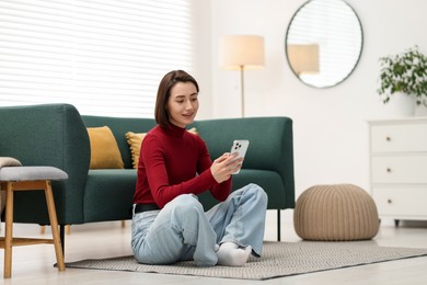 Photo of Woman using modern smartphone on floor at home