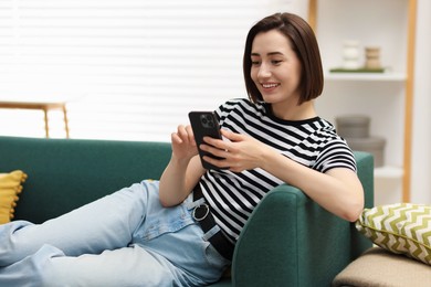 Photo of Woman using modern smartphone on sofa at home. Space for text