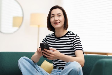 Photo of Woman using modern smartphone on sofa at home