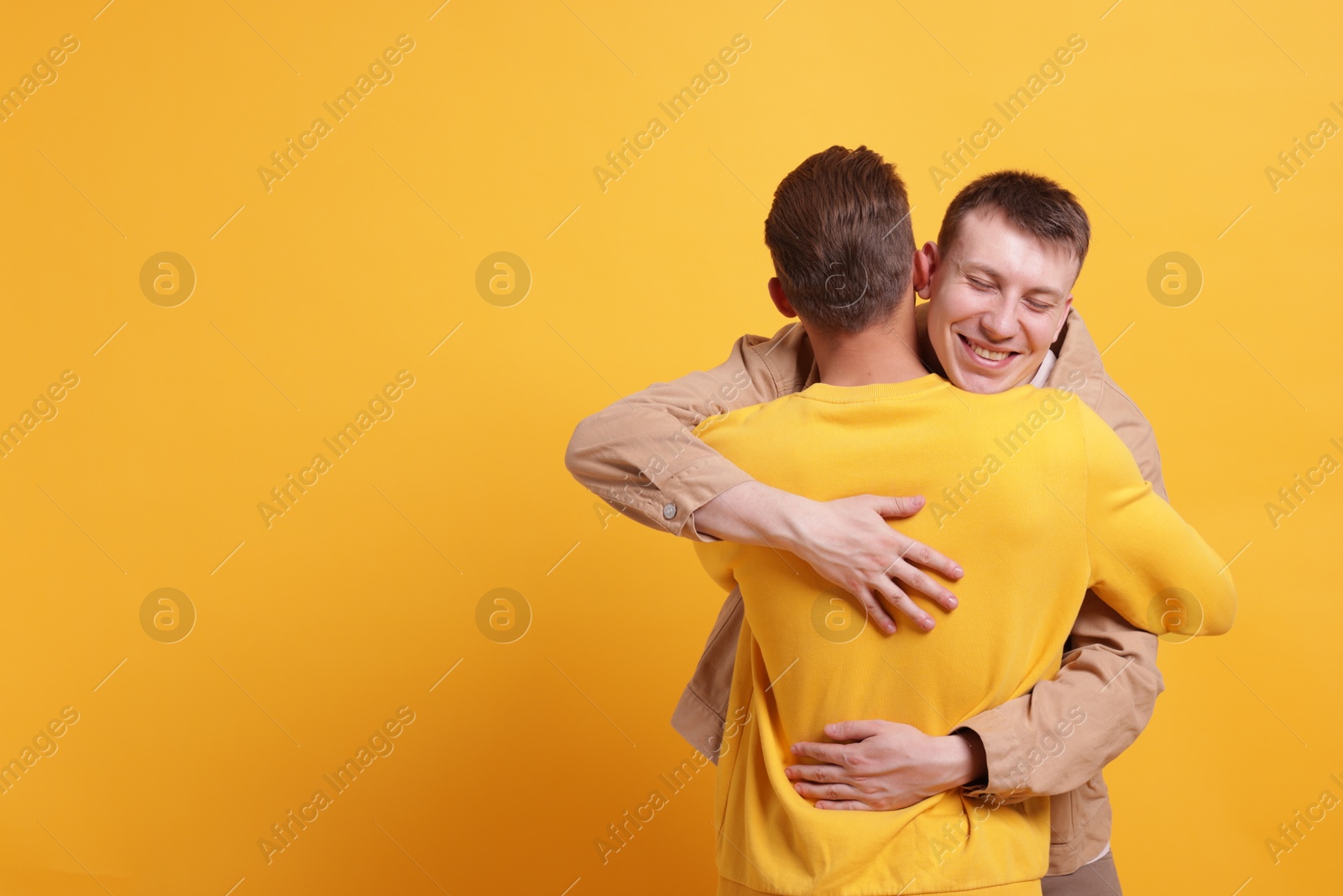 Friends hugging each other on orange background, space for text Photo of Friends hugging each other on orange background, space for text