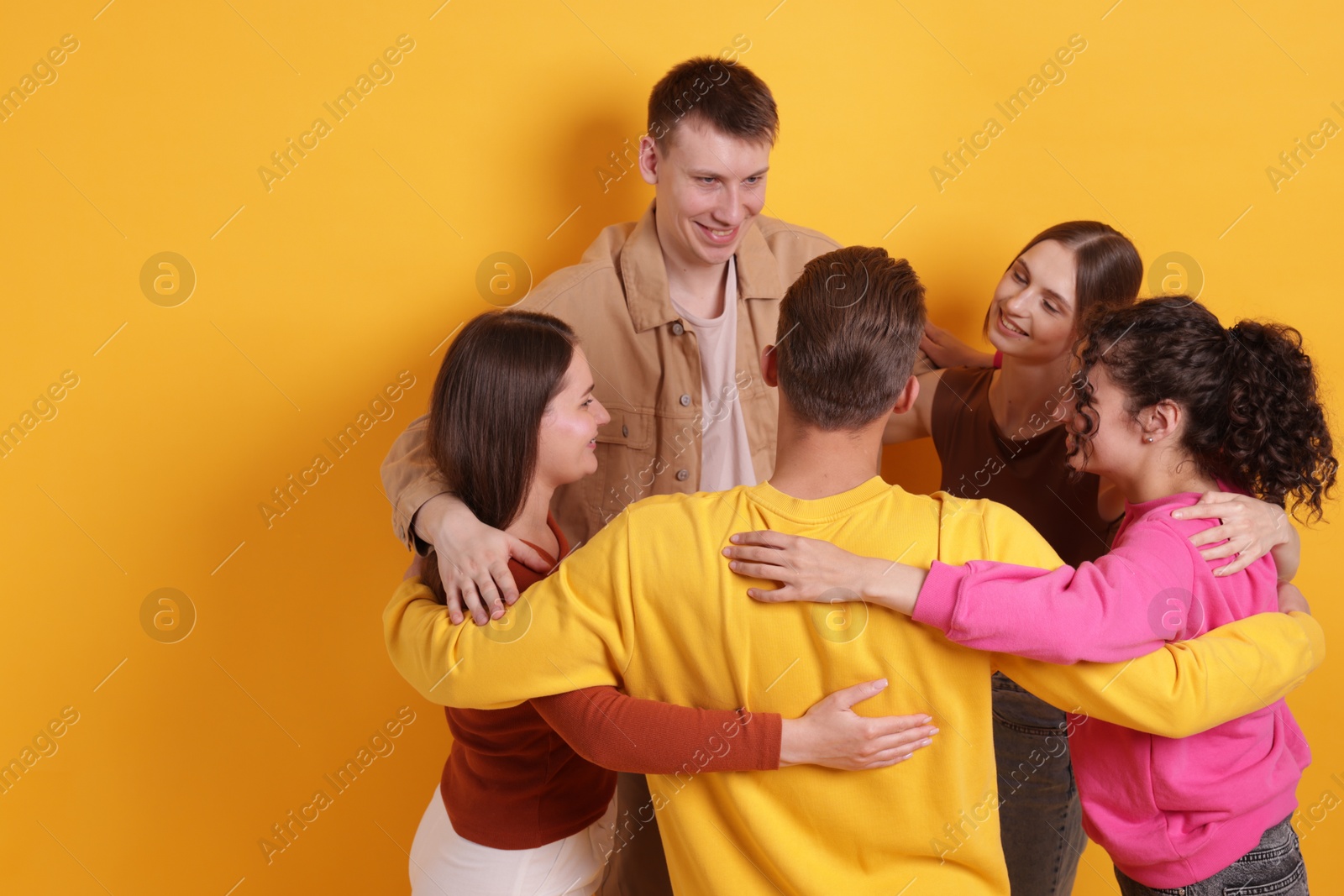 Group of friends hugging each other on orange background, space for text Photo of Group of friends hugging each other on orange background, space for text