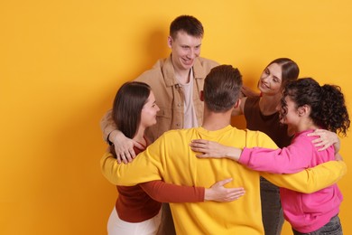 Photo of Group of friends hugging each other on orange background, space for text