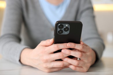 Photo of Woman using smartphone at table indoors, closeup