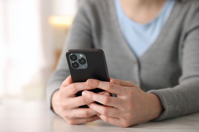Photo of Woman using smartphone at table indoors, closeup
