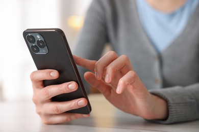 Photo of Woman using smartphone at table indoors, closeup