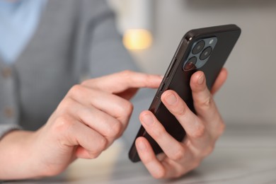 Photo of Woman using smartphone at table indoors, closeup