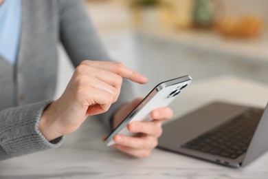 Photo of Woman using modern smartphone at white marble table indoors, closeup