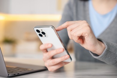 Photo of Woman using modern smartphone at white marble table indoors, closeup