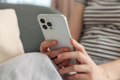 Photo of Woman using modern smartphone on sofa at home, closeup