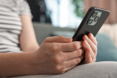 Photo of Woman using modern smartphone on sofa at home, closeup