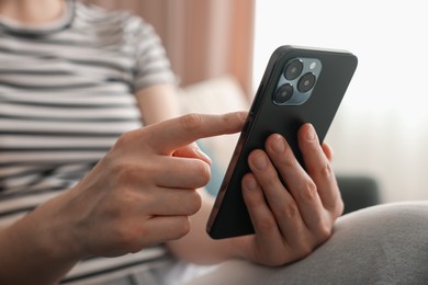 Photo of Woman using modern smartphone at home, closeup